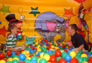 Two boys playing in a colorful ball pit inside an inflatable with cartoon designs at Camping Bella Italia, Veneto.