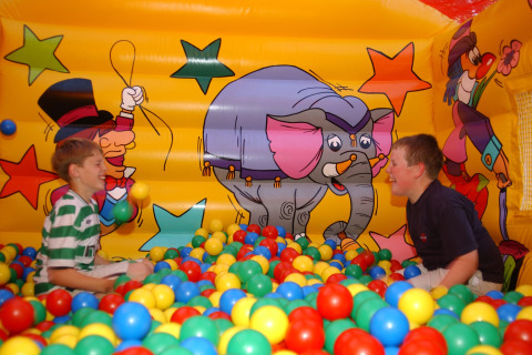Two boys playing in a colorful ball pit inside an inflatable with cartoon designs at Camping Bella Italia, Veneto.