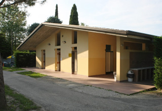 Buiten sanitairgebouw op Camping Bella Italia vakantiepark in Veneto, Italië, omringd door bomen.