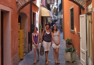 Three women walk along a narrow, colorful alley at Camping Bella Italia, Veneto, Italy, surrounded by charming buildings.