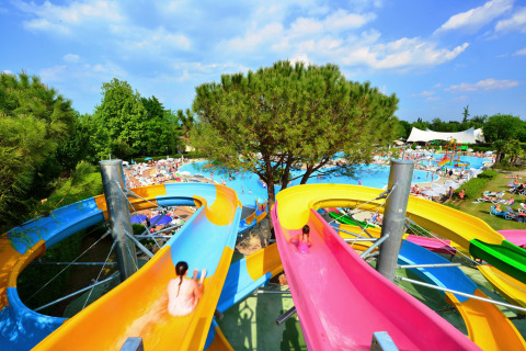 Toboganes de colores en Camping Bella Italia, Veneto, Italia, con piscinas y visitantes al fondo.