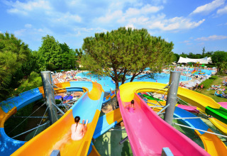 Farverig vandrutsjebane i Camping Bella Italia, Veneto, Italien, med gæster og swimmingpools i baggrunden.