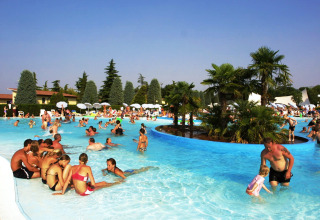 Famiglie e bambini si divertono nella piscina all’aperto tra palme al Camping Bella Italia, Veneto, Italia.