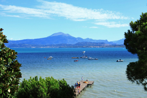 Vista del Lago di Garda da Peschiera del Garda con barche, pontile in legno e montagne sullo sfondo.