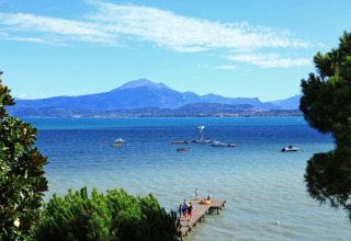 View of Lake Garda from Peschiera del Garda with boats, a wooden pier and mountains in the background.