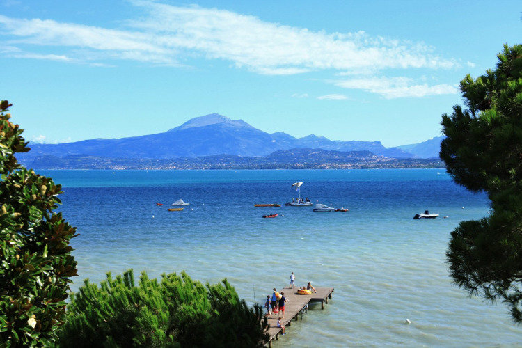 View of Lake Garda from Peschiera del Garda with boats, a wooden pier and mountains in the background.
