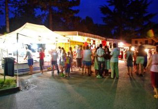 Foto serale di un vivace mercato al Camping Bella Italia in Veneto, Italia, con bancarelle e persone.