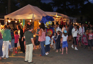 Mercatino serale al Camping Bella Italia in Italia con famiglie, bambini e bancarelle sotto tende illuminate.