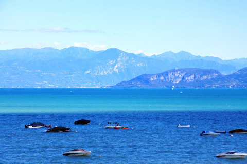Vista sul lago con barche e montagne sullo sfondo, scattata al Camping Bella Italia in Veneto, Italia.