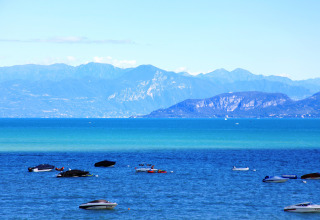 Vista sul lago con barche e montagne sullo sfondo, scattata al Camping Bella Italia in Veneto, Italia.