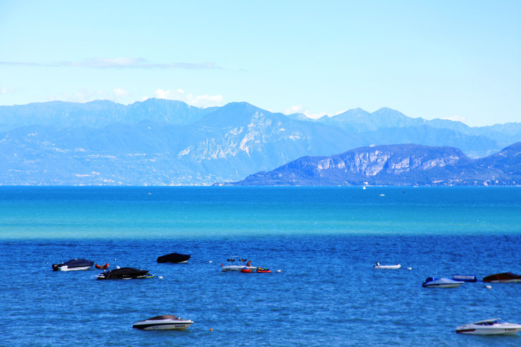 Scenic lake view with boats and mountains in the background, taken at Camping Bella Italia in Veneto, Italy.