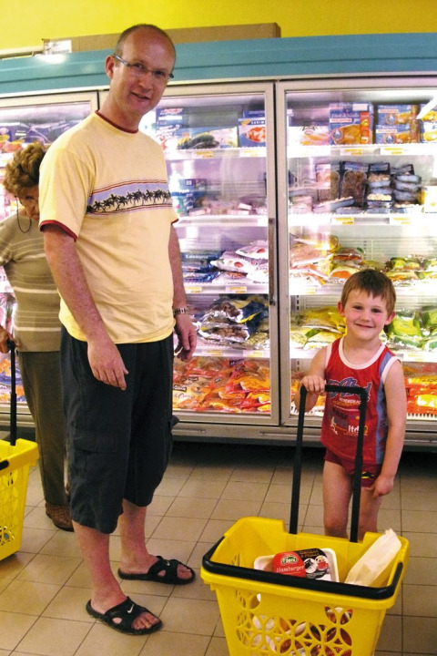 Un hombre y un niño compran en un pasillo de supermercado con congelados, en Camping Bella Italia, Véneto, Italia.
