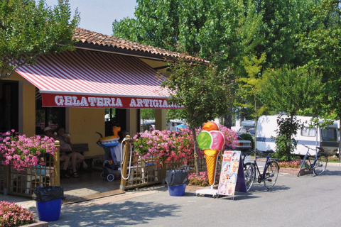 Heladería en Camping Bella Italia en Véneto, Italia, con cartel de helado y bicicletas aparcadas al exterior.