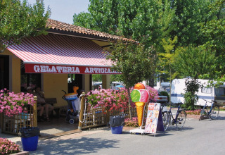 IJssalon bij Camping Bella Italia in Veneto, Italië, met kleurrijke ijsreclame en fietsen buiten in de zomer.