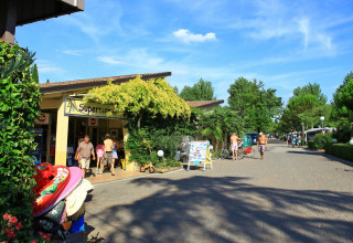 Vacanciers devant le supermarché de Camping Bella Italia, entouré de verdure à Vénétie, Italie.
