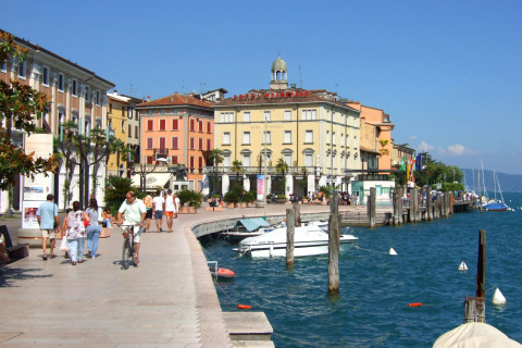 Waterfront promenade in Veneto, Italy, with people walking, colorful buildings, and boats on a sunny day.
