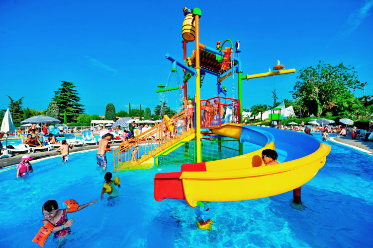 Children play in a colorful water park with a slide at Camping Bella Italia holiday park in Veneto, Italy.