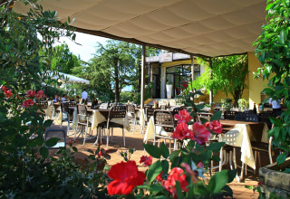 Udendørs restaurant med borde dækket af duge og blomster i forgrunden på Camping Bella Italia i Veneto.