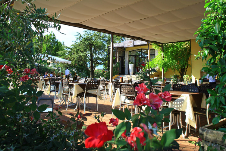 Outdoor restaurant with tables and flowers in the foreground at Camping Bella Italia holiday park in Veneto.