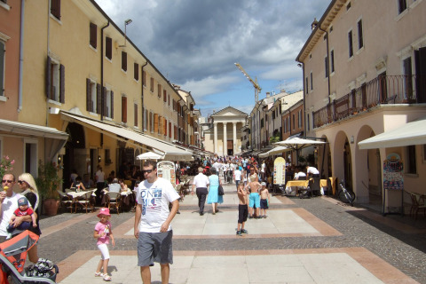 Busy pedestrian street at Camping Bella Italia, Veneto, Italy, lined with cafés, shops, and people enjoying summer.