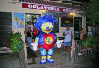 En person i et farverigt maskotkostume foran en gelateria på campingpladsen Bella Italia i Veneto, Italien.