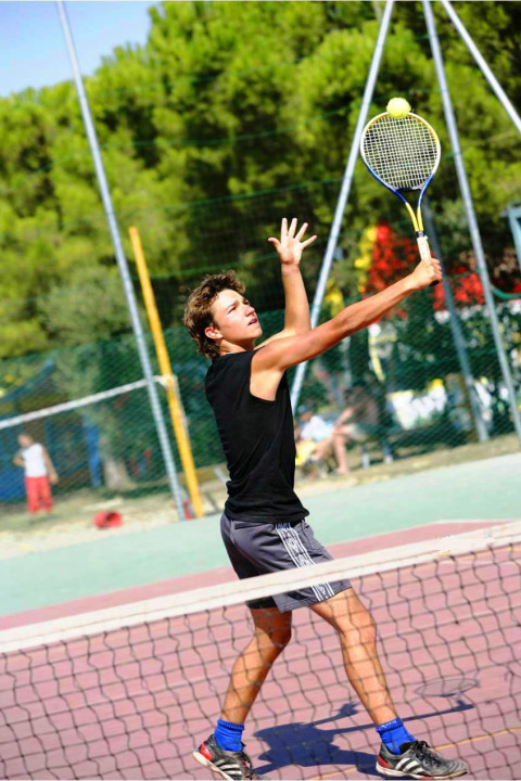 Joven jugando al tenis en el Camping Bella Italia, un parque vacacional en Véneto, Italia, realizando un saque.
