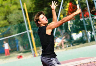 Giovane che gioca a tennis al Camping Bella Italia, villaggio vacanze in Veneto, Italia, durante un servizio.