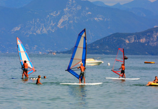 Persone che fanno windsurf su un lago con montagne sullo sfondo a Camping Bella Italia, Veneto, Italia.