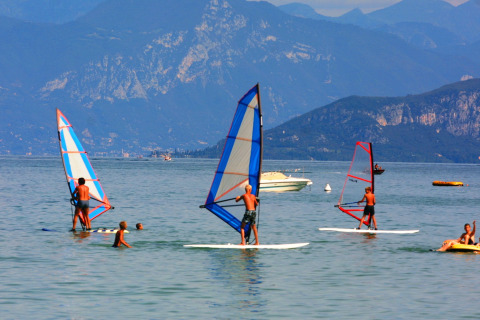 Des personnes font de la planche à voile sur un lac avec des montagnes à l’arrière-plan à Camping Bella Italia, Vénétie, Italie.