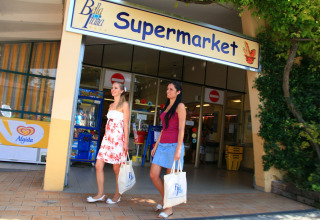 Two women leaving a supermarket at Camping Bella Italia holiday park in Veneto, Italy, on a sunny day.