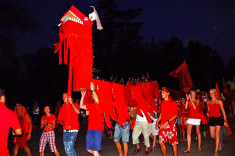 Personas vestidas de rojo llevan un dragón gigante en un desfile nocturno en Camping Bella Italia, Véneto, Italia.
