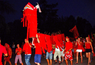 Persone in rosso trasportano un drago durante una sfilata notturna al Camping Bella Italia in Veneto, Italia.