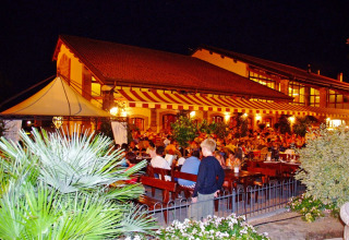 Outdoor restaurant area at Camping Bella Italia in Veneto, Italy, crowded with people and evening lights.