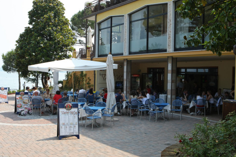 Area pranzo esterna al Camping Bella Italia in Veneto, Italia, con persone sedute ai tavoli sotto gli ombrelloni.