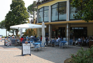 Area pranzo esterna al Camping Bella Italia in Veneto, Italia, con persone sedute ai tavoli sotto gli ombrelloni.