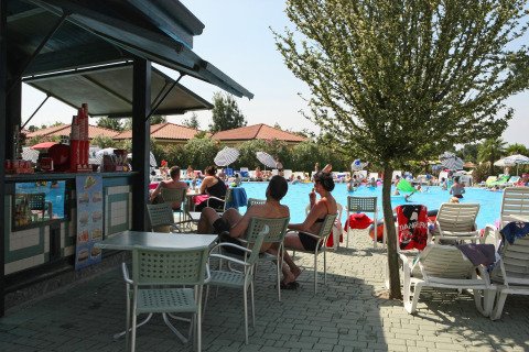 Ospiti rilassati vicino alla piscina e al bar del Camping Bella Italia, villaggio vacanze in Veneto, Italia.