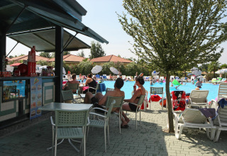 Ospiti rilassati vicino alla piscina e al bar del Camping Bella Italia, villaggio vacanze in Veneto, Italia.