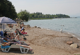 Holidaymakers relaxing on loungers by the lakeside at Camping Bella Italia, Veneto, Italy, on a sunny day.