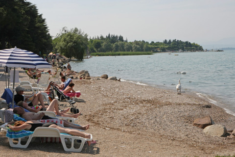 Villeggianti che si rilassano sui lettini a bordo lago a Camping Bella Italia, Veneto, Italia, in una giornata soleggiata.