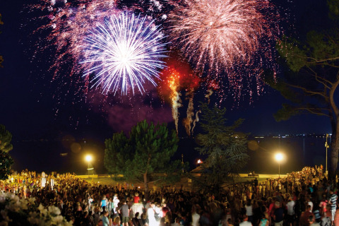 Fuochi d'artificio colorati illuminano il cielo notturno sopra una folla al Camping Bella Italia in Veneto.