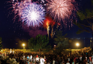 Fuochi d'artificio colorati illuminano il cielo notturno sopra una folla al Camping Bella Italia in Veneto.