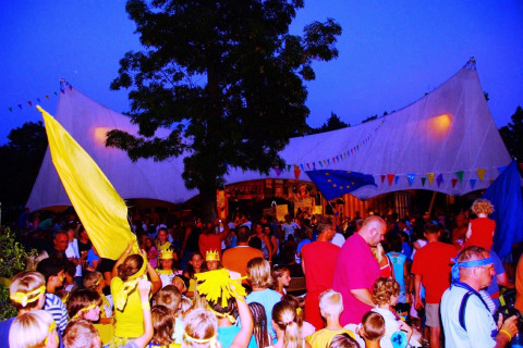 Families with children celebrate under colorful flags at Camping Bella Italia holiday park in Veneto, Italy.