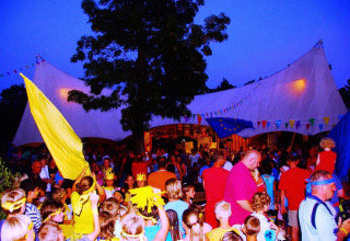 Families with children celebrate under colorful flags at Camping Bella Italia holiday park in Veneto, Italy.