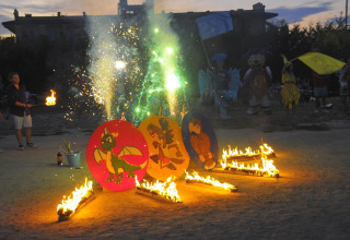 Children and adults enjoy an evening event with fire, fireworks, and mascots at Camping Bella Italia.