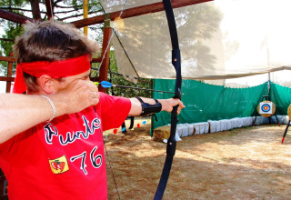 A person wearing a red headband shoots a bow at an archery range in Camping Bella Italia, Veneto, Italy.