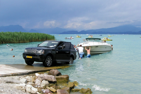 Un Range Rover saca un barco del agua en Camping Bella Italia, Véneto, Italia. Personas ayudan en la orilla.