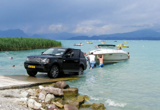 En Range Rover trækker en båd op af vandet på Camping Bella Italia i Veneto, Italien. Folk hjælper ved søen.