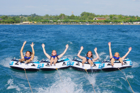 Cuatro chicas disfrutan de tubing acuático en Camping Bella Italia, Veneto, Italia, con las manos en alto.