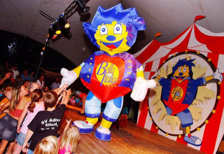 Niños rodean a una colorida mascota en el escenario durante un espectáculo en Camping Bella Italia, Véneto, Italia.
