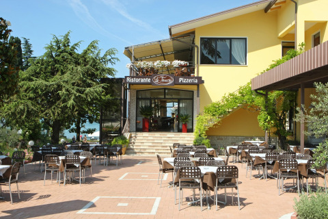 Zona exterior de restaurante en el camping Bella Italia en Véneto, Italia, con mesas y sillas al aire libre.